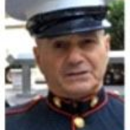 Man in Marine Corps uniform, staring forward. Navy blue jacket with red trim, white hat.