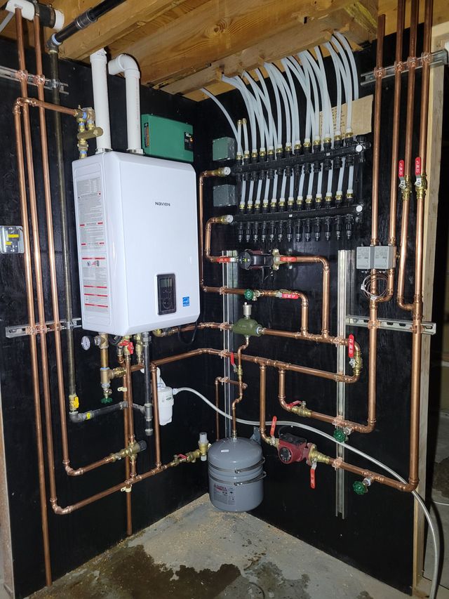 Copper pipes and white water heater in a mechanical room, connected to a black manifold system.