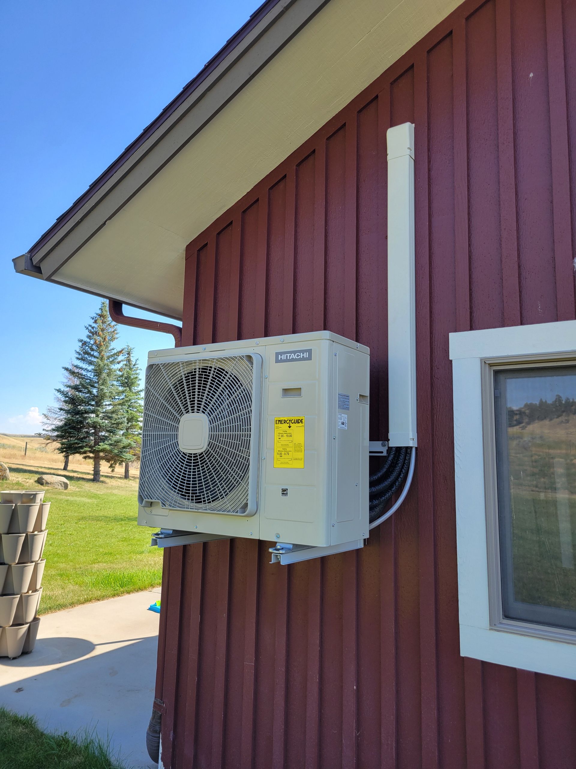 Exterior heat pump unit mounted on a red building wall, with white pipe and a small window.