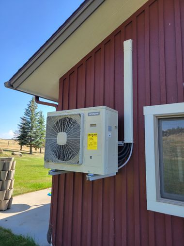 Exterior heat pump unit mounted on a red building wall, with white pipe and a small window.