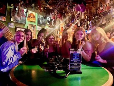 Three women in cowboy hats are sitting at a table in a bar.