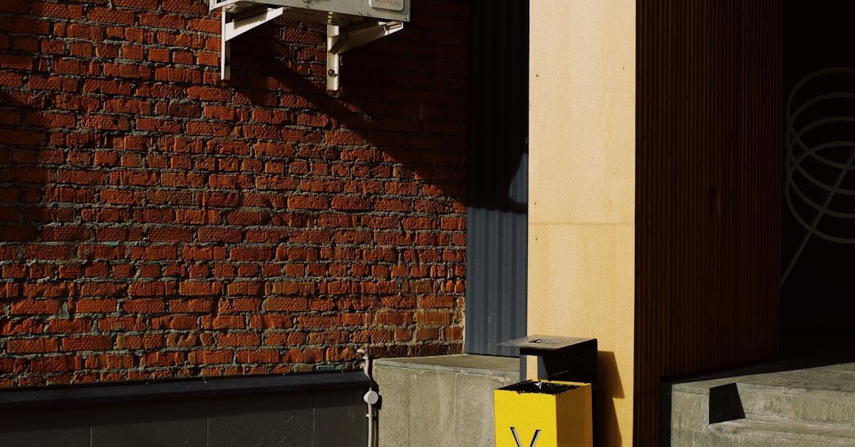 Brick wall beside a concrete ledge, wood panel, and yellow caution sign in an urban alleyway.