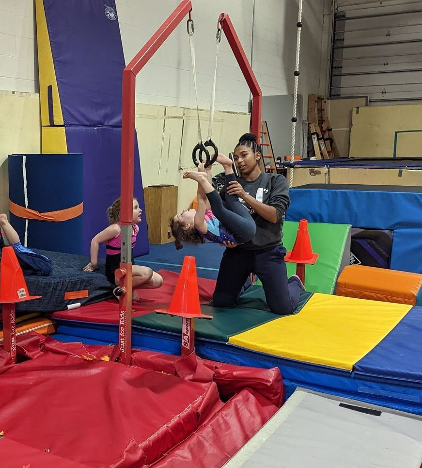 A woman is helping a young girl do a trick on a gymnastics bar