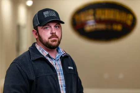 Man in black cap and jacket standing indoors, with a blurred oval sign in the background