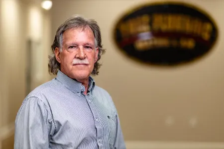 Man in a patterned shirt standing indoors with a blurred wall sign in the background