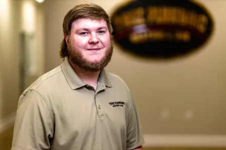 Smiling man in a tan polo shirt standing indoors with a blurred sign in the background