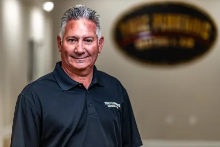 Man standing in a black polo shirt indoors, smiling in front of a blurred wall sign.