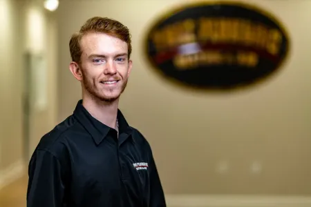 Smiling man in a black shirt standing in an office hallway with a blurred sign behind him