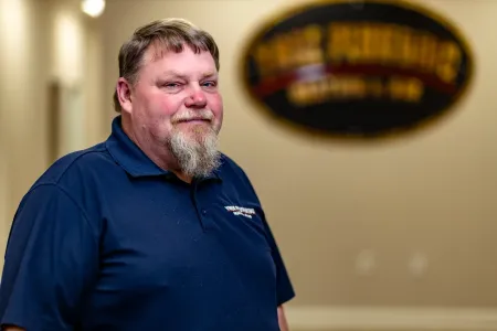 Man in a blue polo shirt standing indoors with a blurred sign in the background