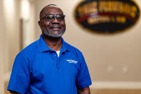 Man in blue polo shirt smiling in a hallway, with a blurred wall sign in the background