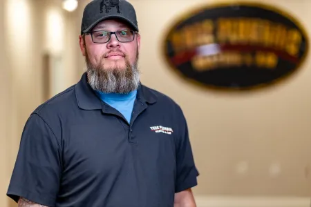 Man in a dark polo and cap standing indoors with a blurred sign in the background