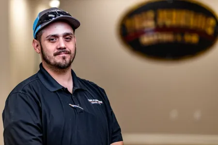 Man in a black shirt and cap standing indoors with a blurred sign in the background