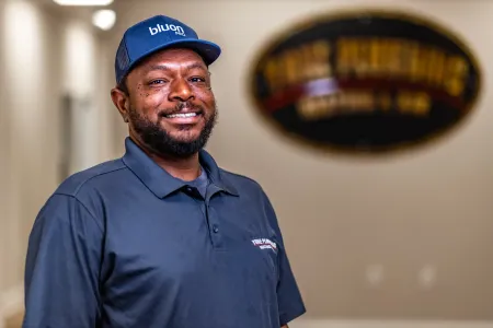 Smiling man in a blue polo and cap standing indoors with a blurred sign in the background