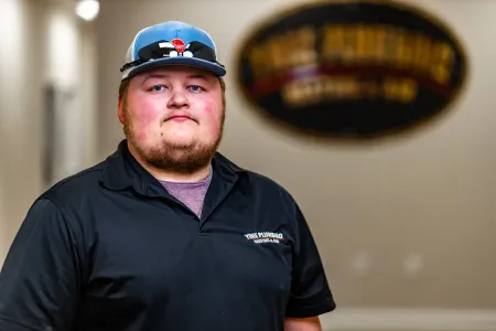 Man standing in a black polo and blue cap in a hallway with a blurred wall sign behind him