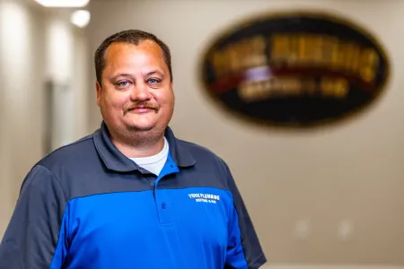 Man in a blue polo shirt standing indoors with a blurred office sign in the background