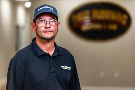 Man in a black polo and cap standing indoors with a blurred oval wall sign behind him