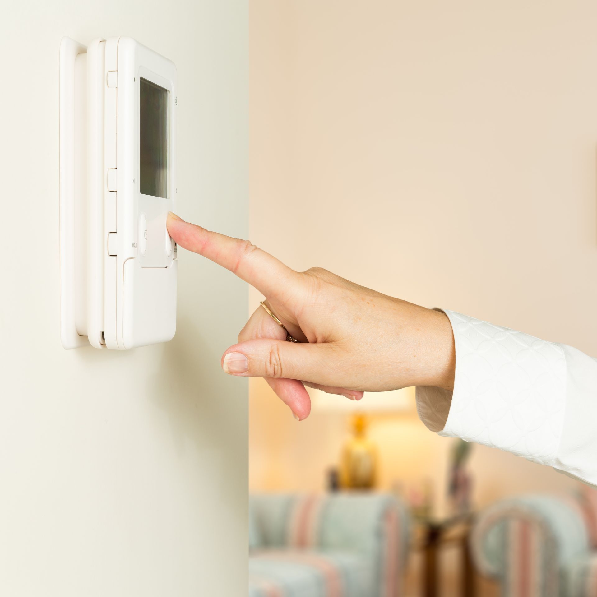 Woman kneels in a living room, using a smartphone beside a white air purifier near a couch.
