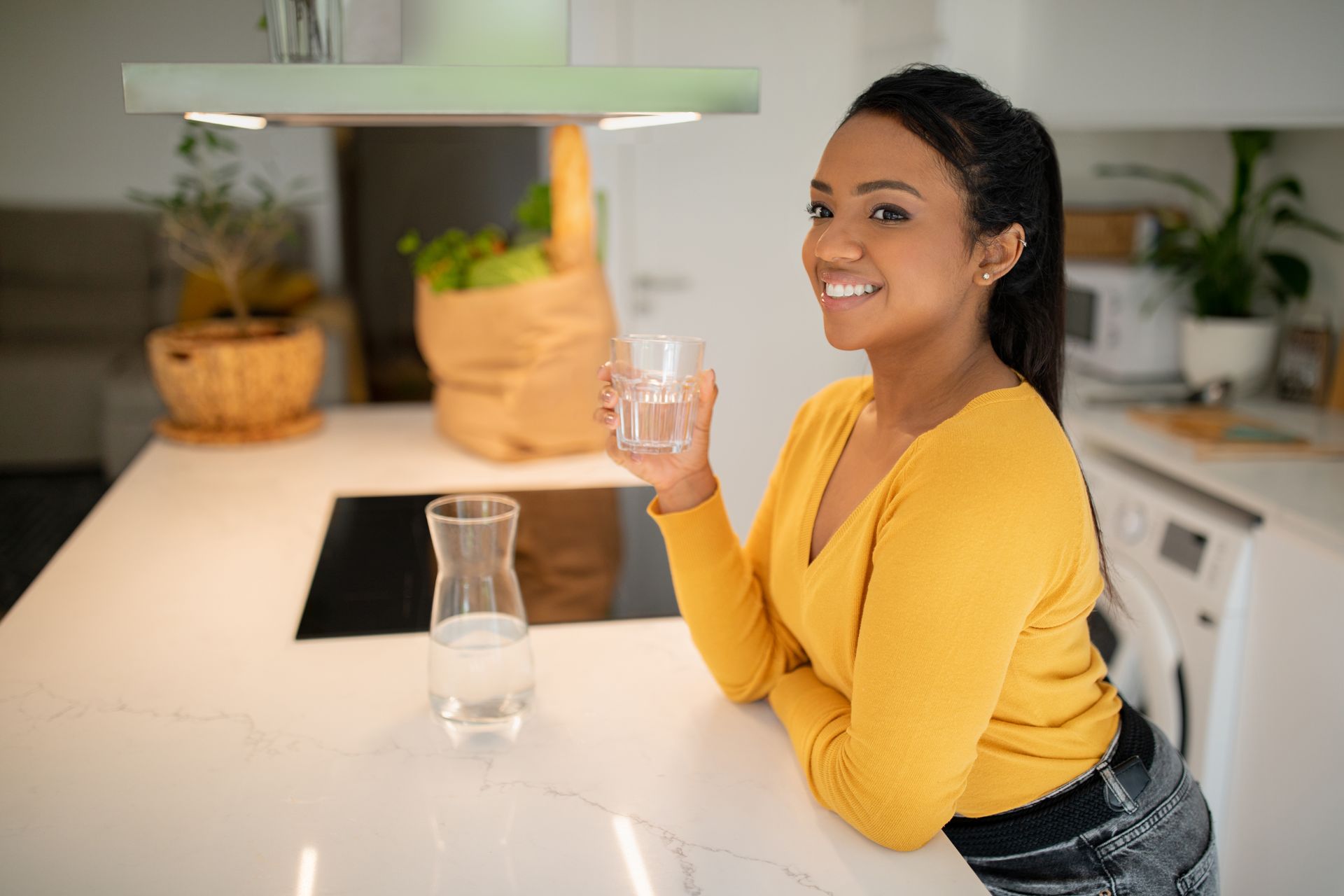 Woman kneels in a living room, using a smartphone beside a white air purifier near a couch.