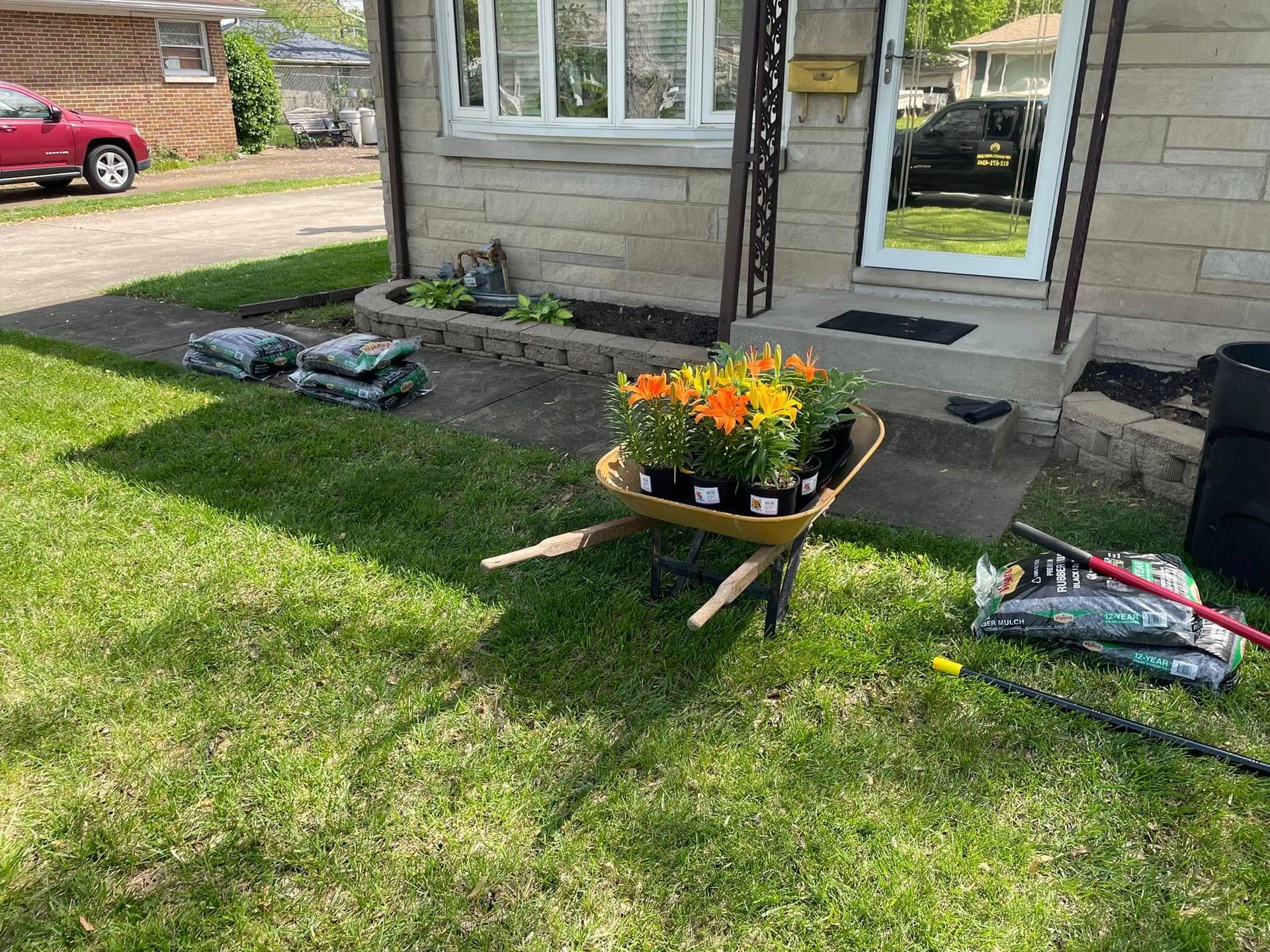Wheelbarrow with orange flowers, bags of soil, and a house with a small garden.