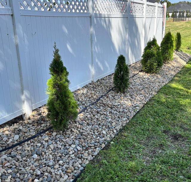 Man in neon shirt mowing grass with yellow zero-turn mower near a tree.