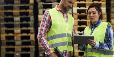 A man and a woman are standing in a warehouse looking at a tablet.