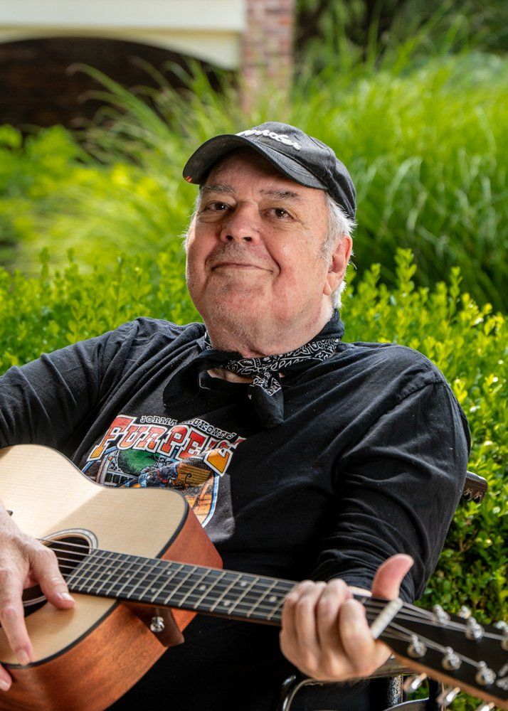 a man is sitting in a wheelchair holding a guitar, Jeff Dunlap, writer, PR person, and musician getting ready to perform at an outdoor concert in Webster Groves, Missouri.