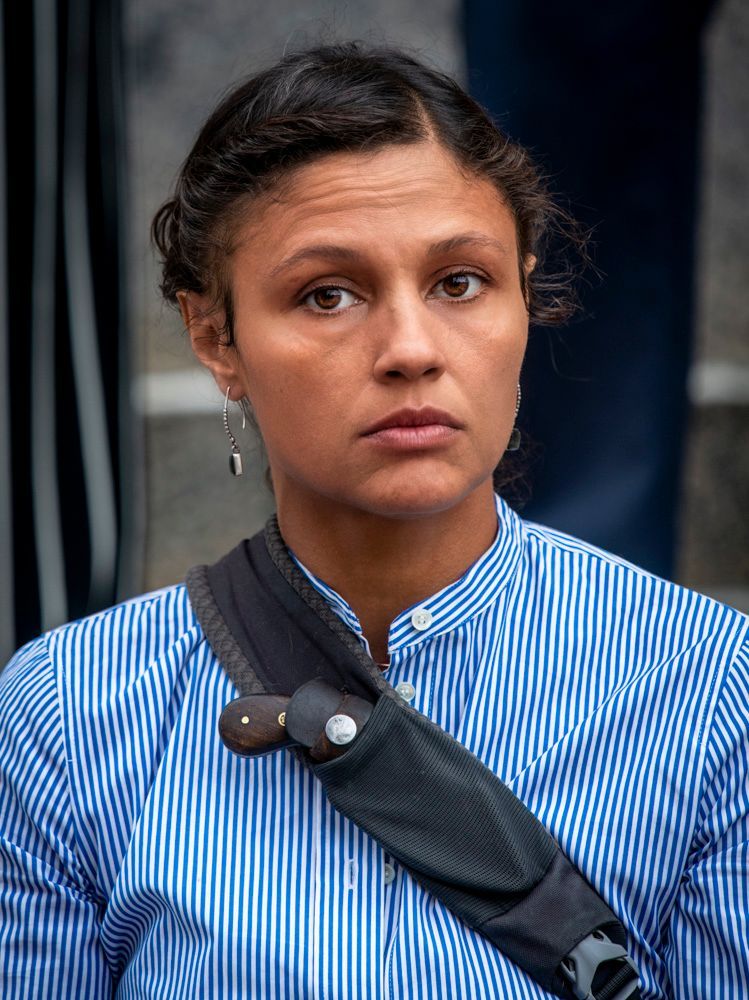a woman wearing a blue and white striped shirt has a black strap around her shoulder, activist, friend of mother of fatal state violence victim, attending memorial for the son in downtown St. Louis.