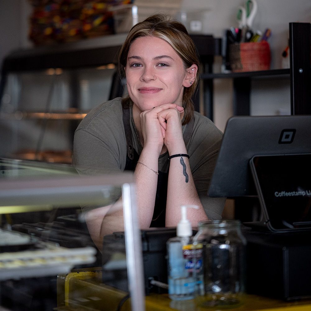 woman, a female barrister behind a counter with a computer that says Coffeestamp on it, beautiful smile