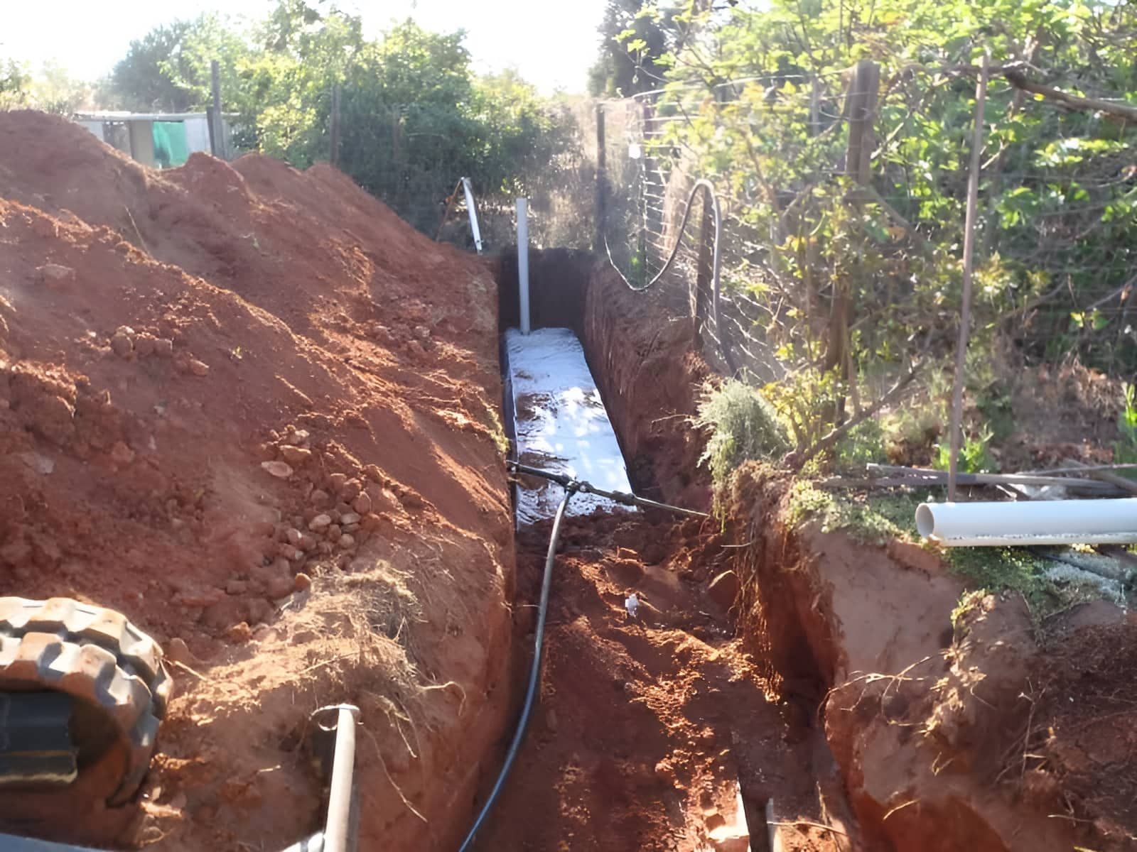 An Excavator Is Digging A Hole In The Dirt Next To A Ladder — Araluen Plumbing In Braitling, NT