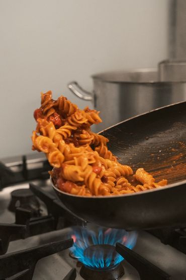 Pasta saltata da una padella nera su una fiamma a gas blu in una cucina