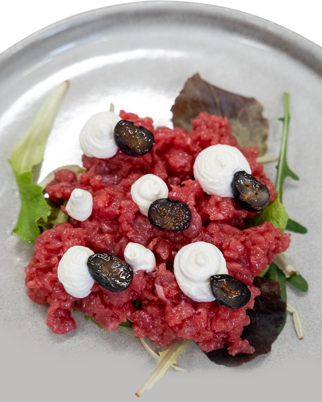 Tartare di manzo crudo macinato, guarnita con ciuffi bianchi e capperi scuri, servita su un piatto di metallo.