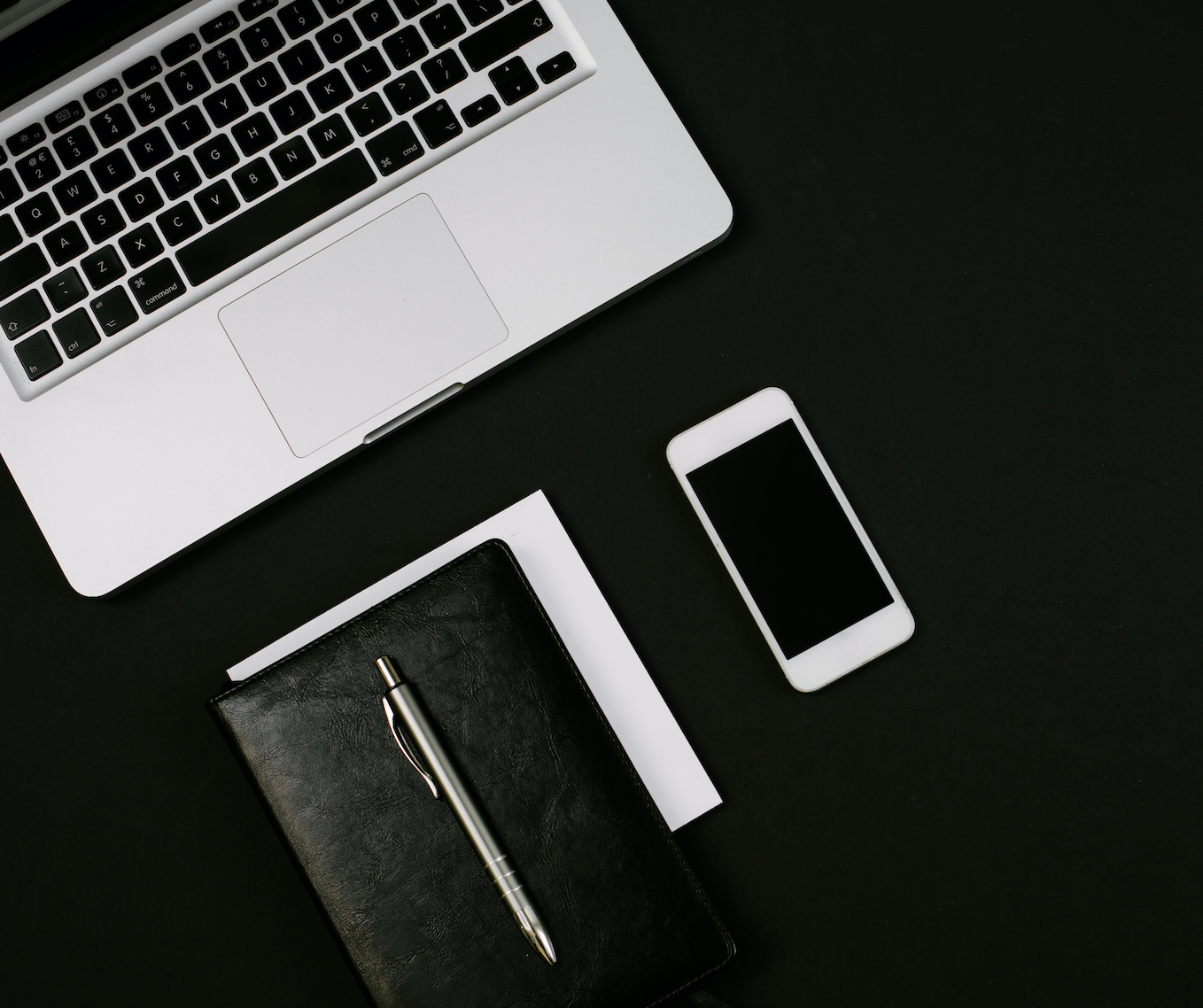 A laptop , cell phone , notebook and pen on a black table