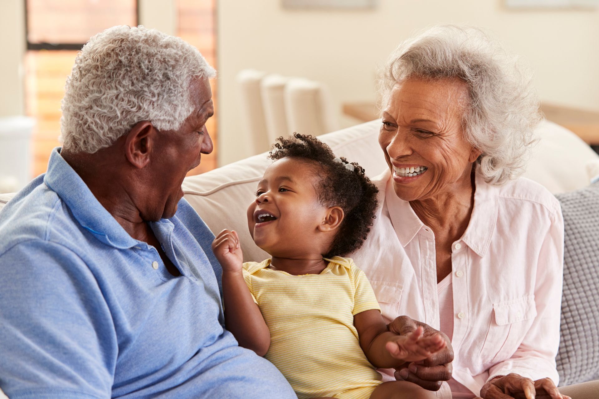 A child sits on a couch between two people who are looking at them, all three smiling and engaged in conversation.