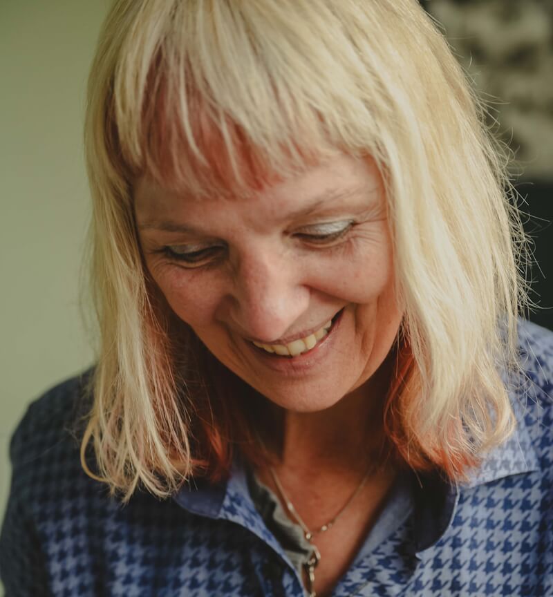 Een vrouwelijke kunstenaar met blond haar lacht terwijl zij wordt gefotografeerd