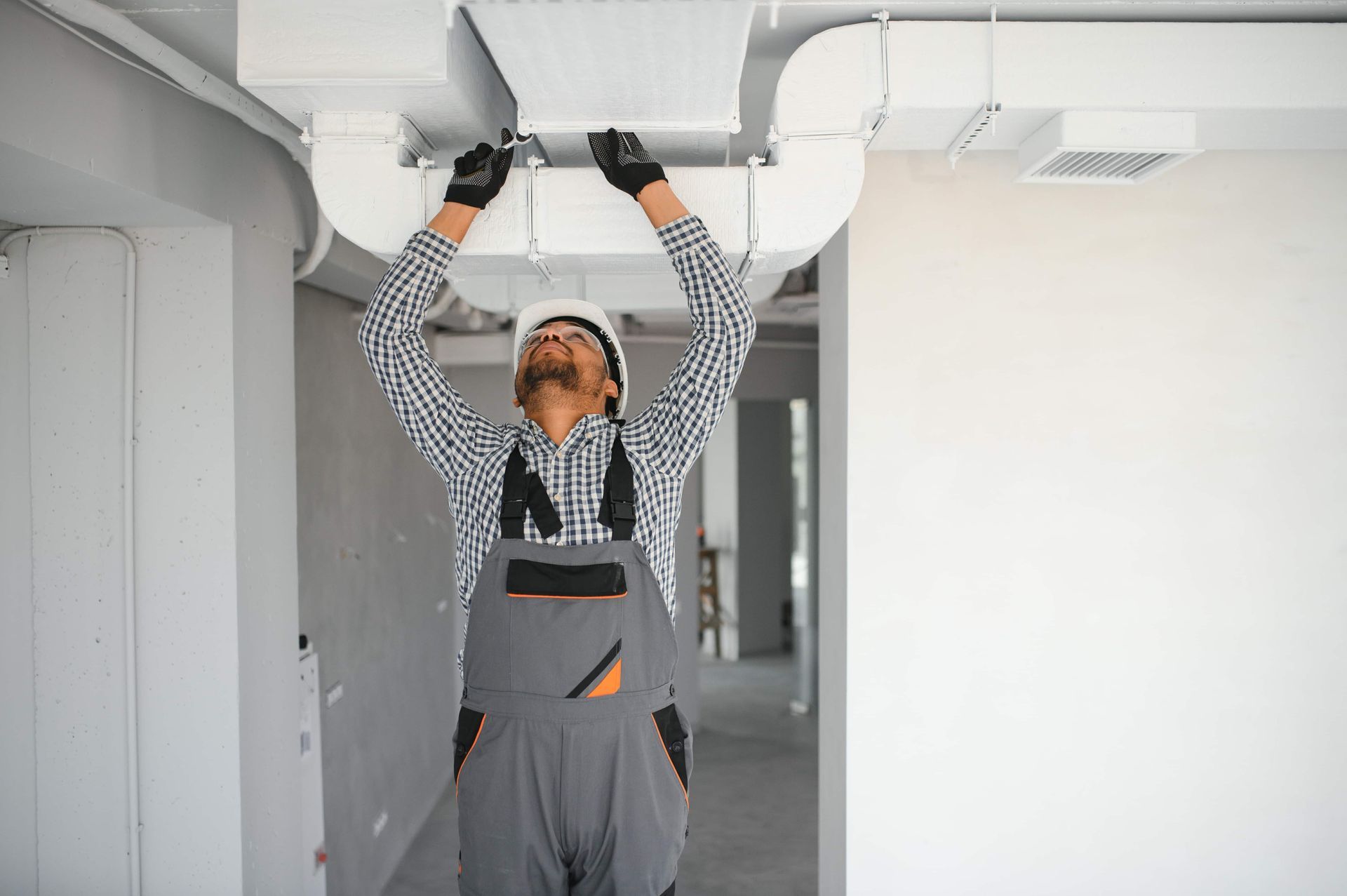 A man is working on a ventilation system on the ceiling of a building.