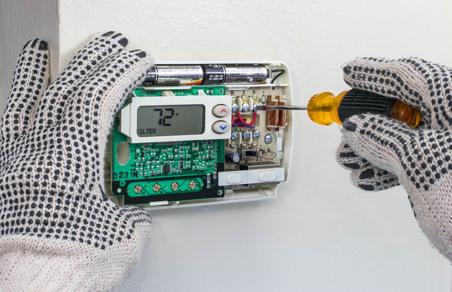 A person is fixing a thermostat with a screwdriver.