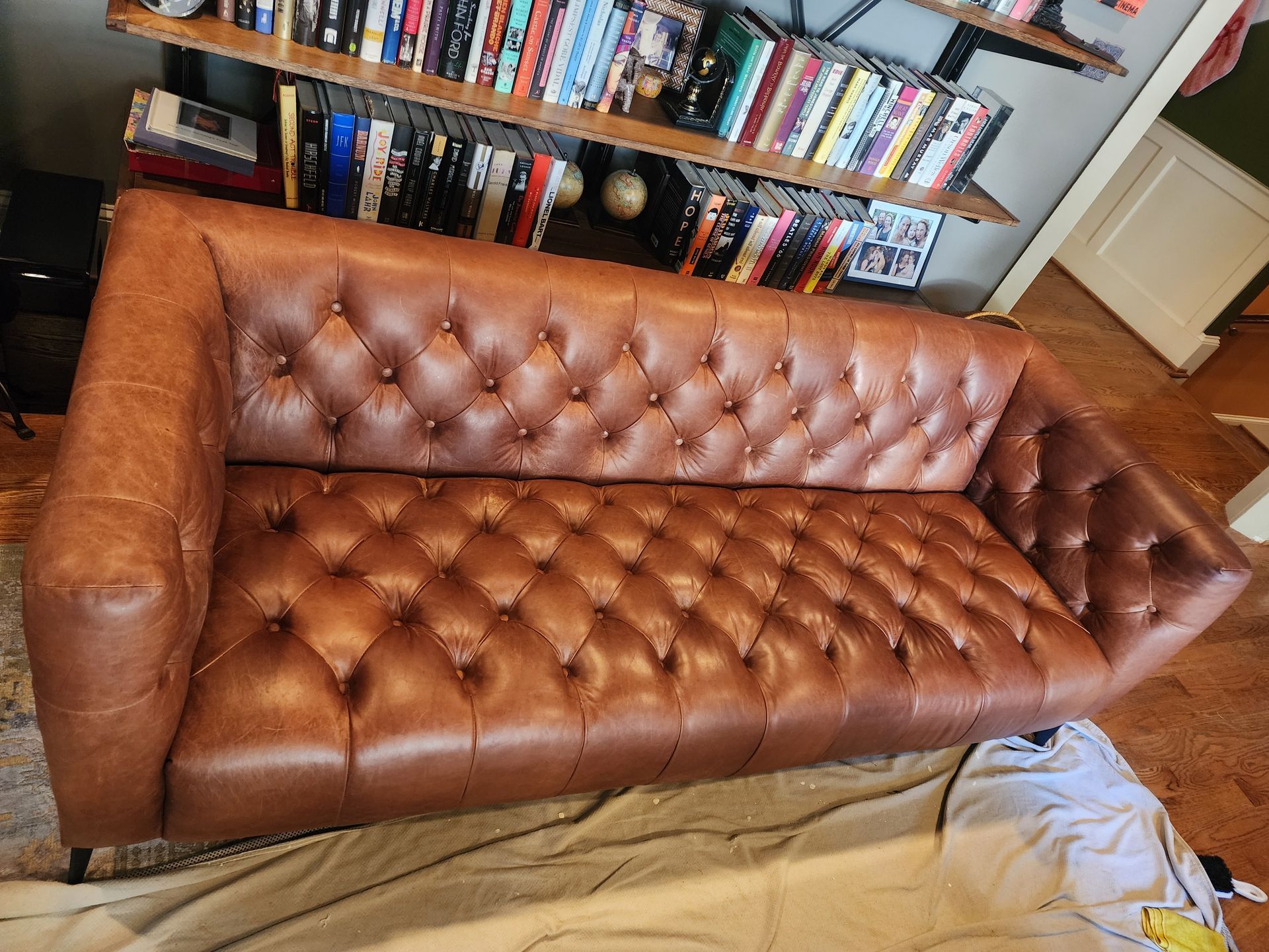 Brown tufted leather sofa in a room with bookshelves in the background.