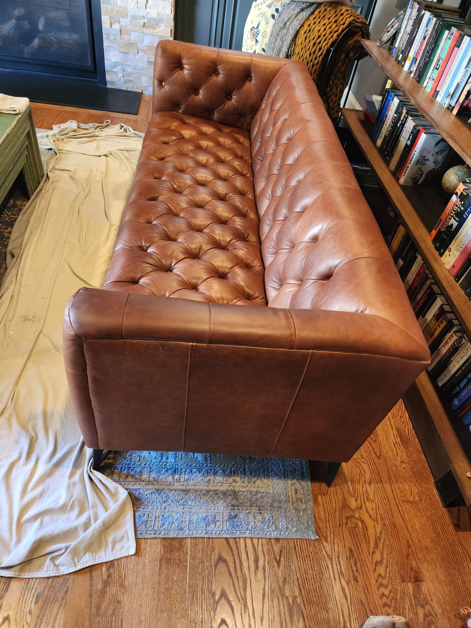 Brown tufted leather sofa in a room with hardwood floor and bookshelves.