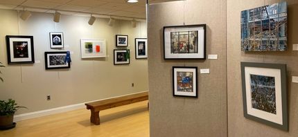 Art gallery with paintings on white walls, geometric ceiling, people viewing artwork.