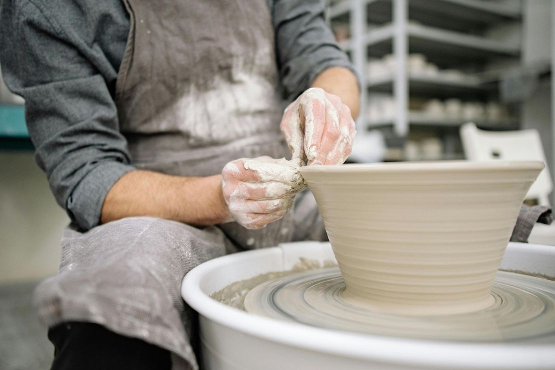 Potter shaping clay bowl on a spinning wheel; hands covered in clay in a pottery studio.