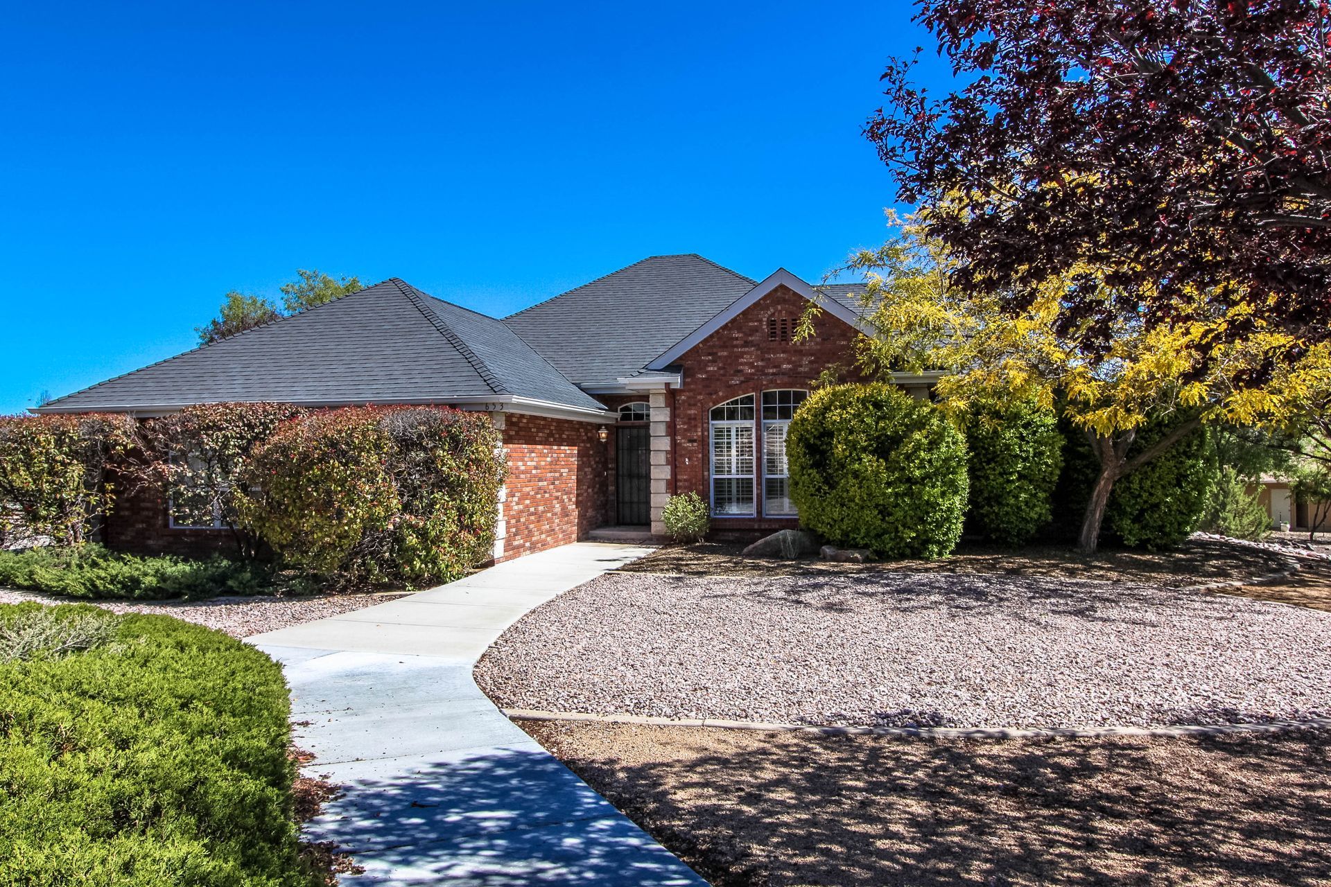A brick house with a black roof and a concrete walkway leading to it.