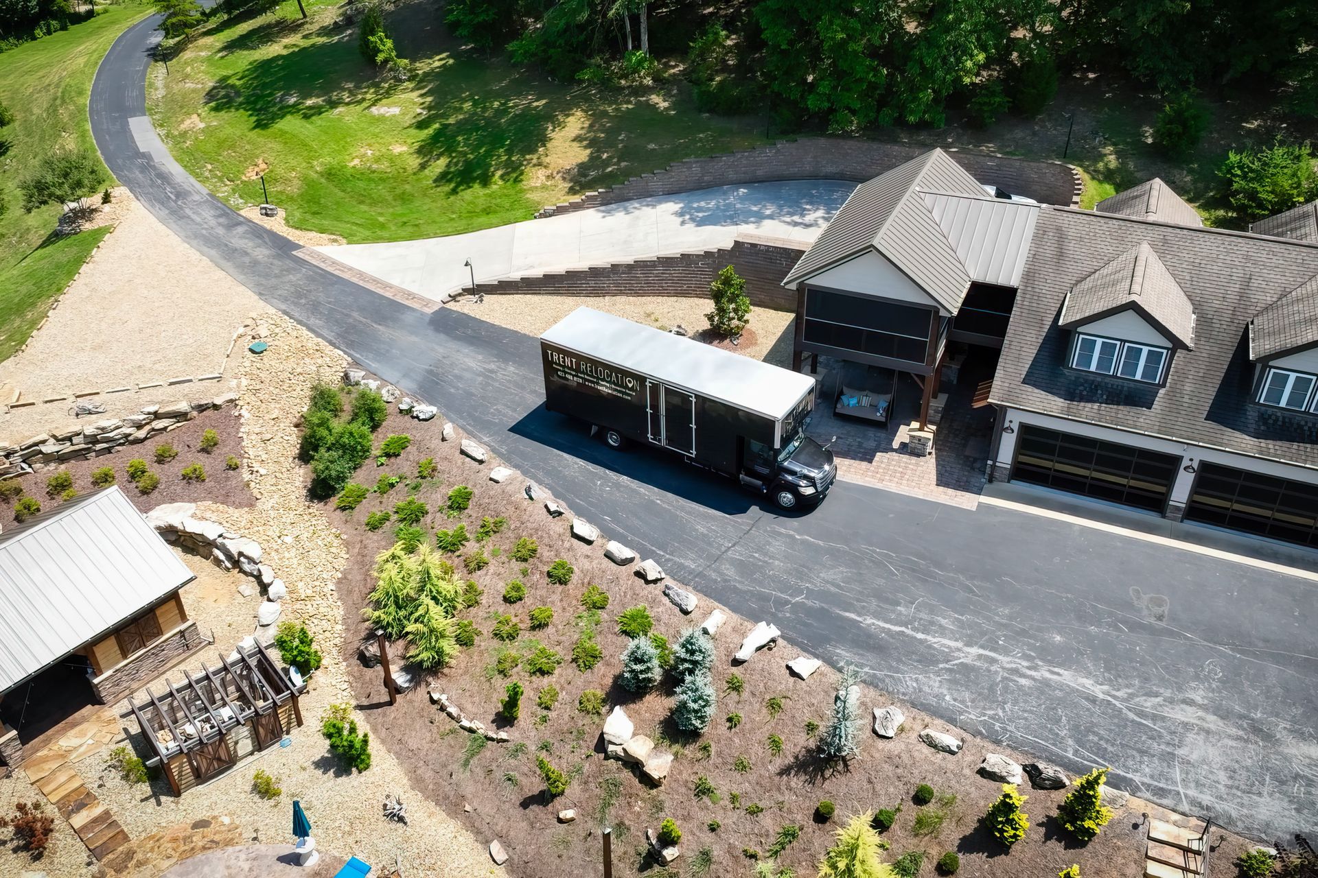 Black trailer truck on driveway near house with brown roof and landscaping.