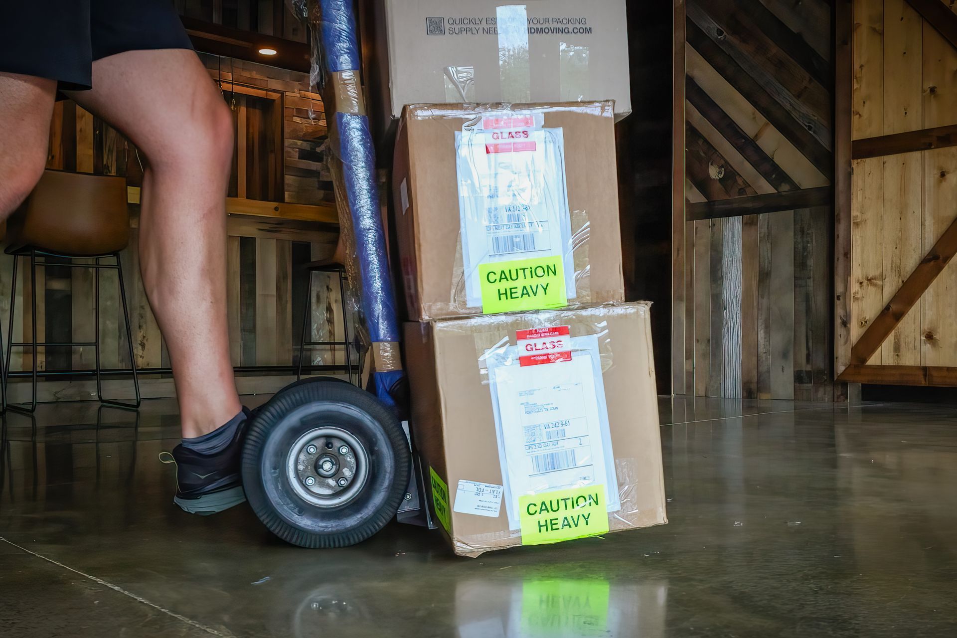 Person using a hand truck to move stacked cardboard boxes labeled