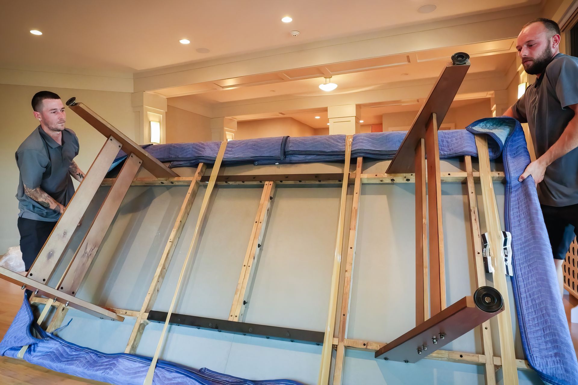 Two men lifting a large, blue upholstered couch. The frame is wooden, indoors.