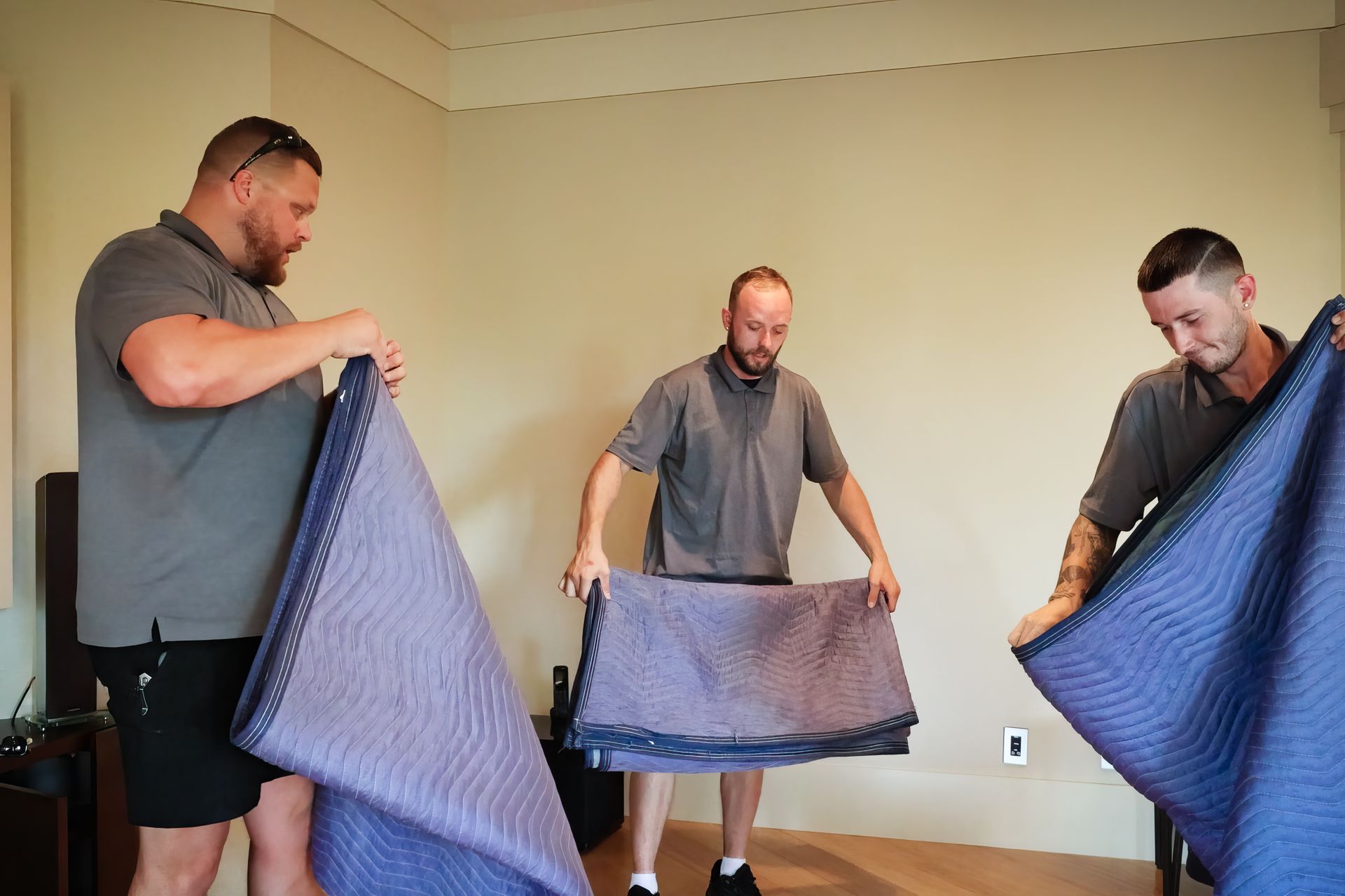 Person wrapping a white couch with clear plastic wrap. Dark shorts, black shoes, and blue wall in the background.
