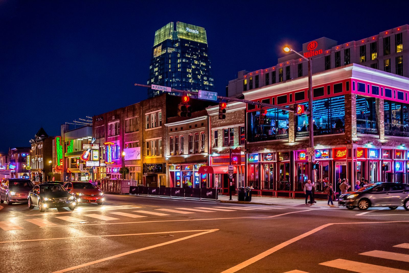 Nashville skyline at dusk with river reflection. Buildings and bridge lit up against a colorful sky.