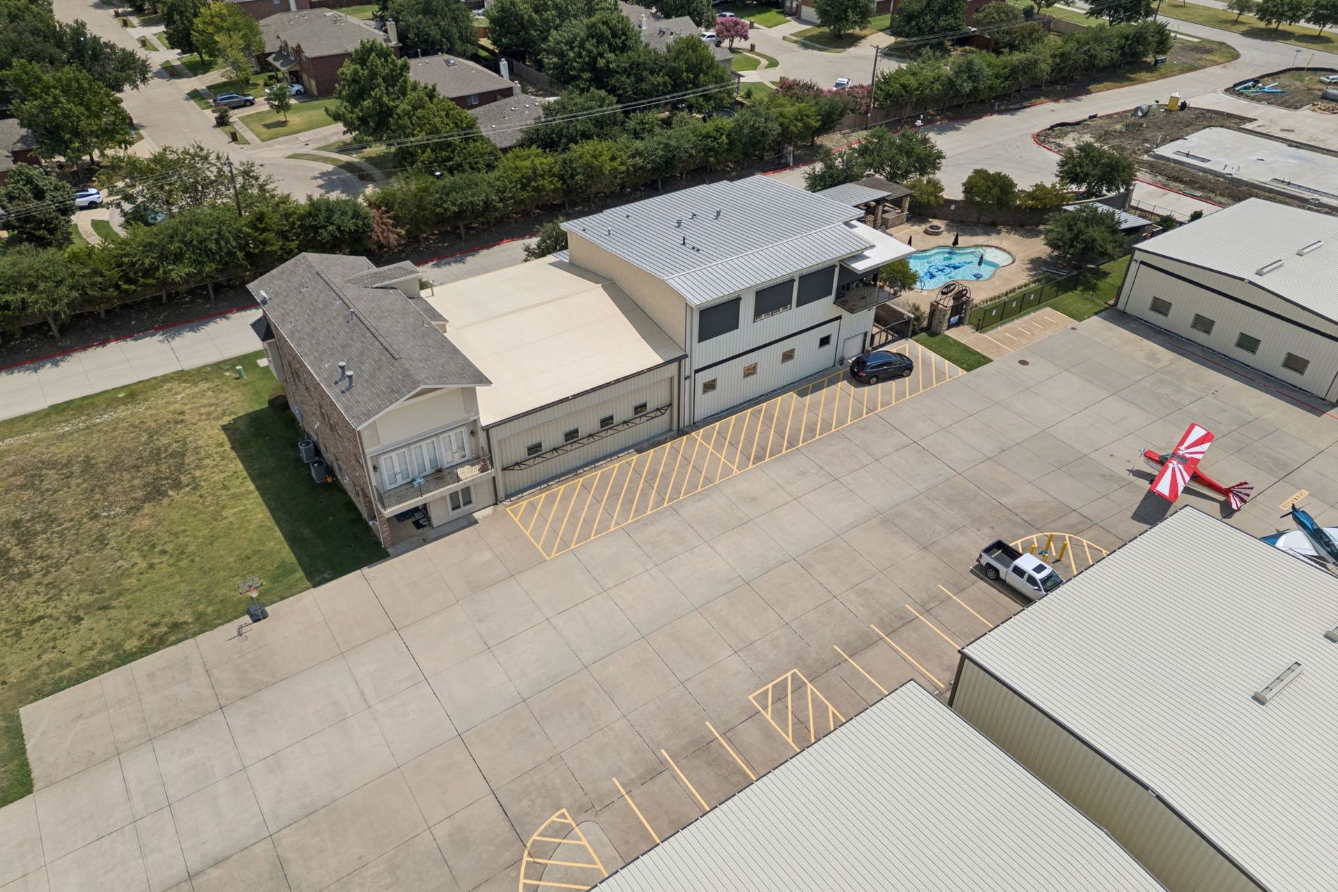 Aerial view of a parking lot beside buildings, with a small pool and trees nearby.