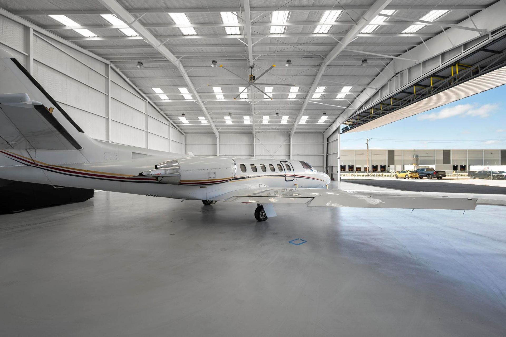 Small white business jet parked inside a bright hangar with its nose facing left.