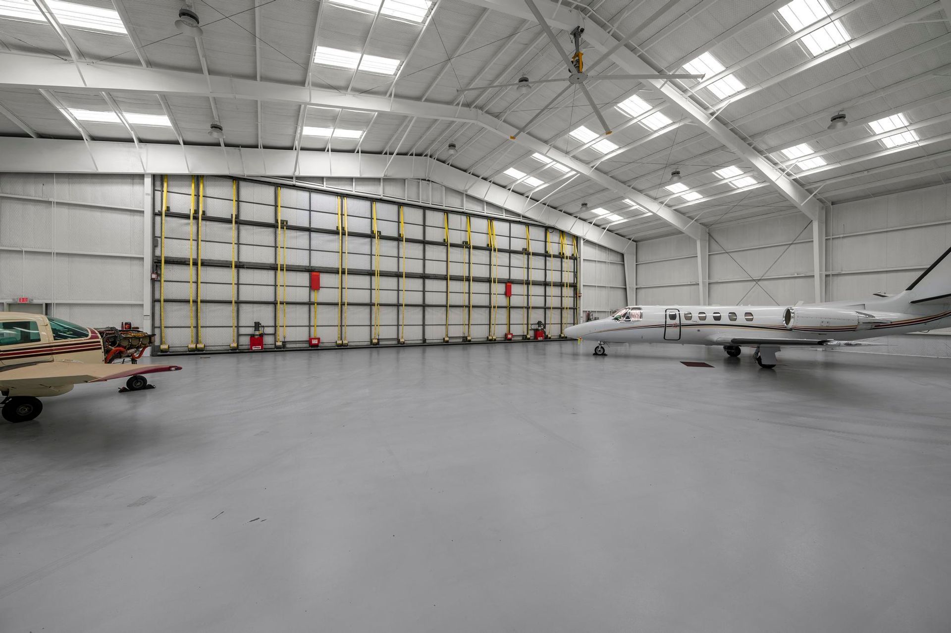 Large aircraft hangar with a white plane, maintenance equipment, and a high arched ceiling