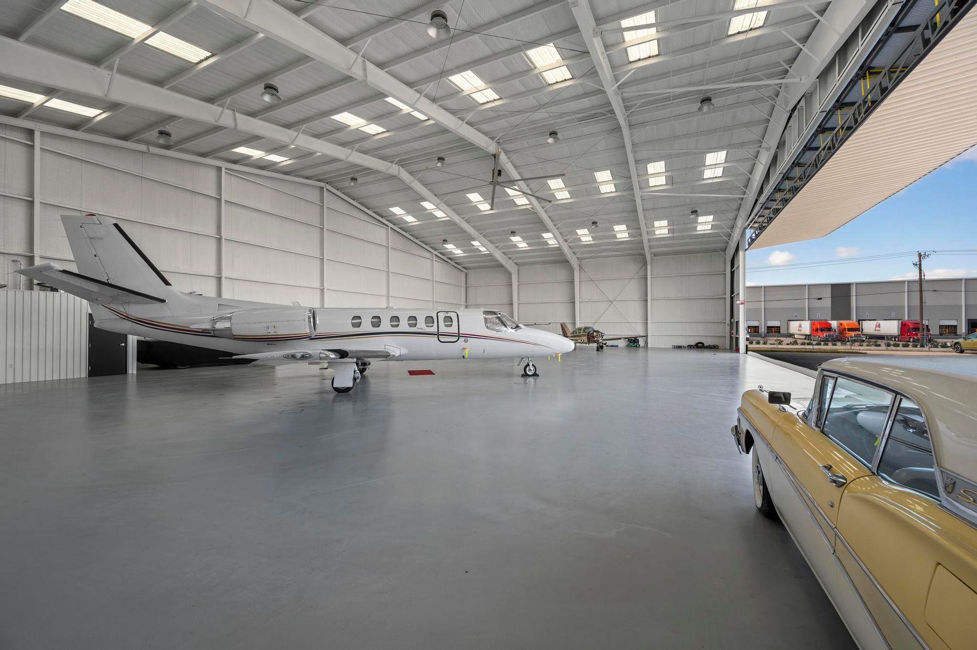 Small airplane in a hangar beside a gold car under a high white roof